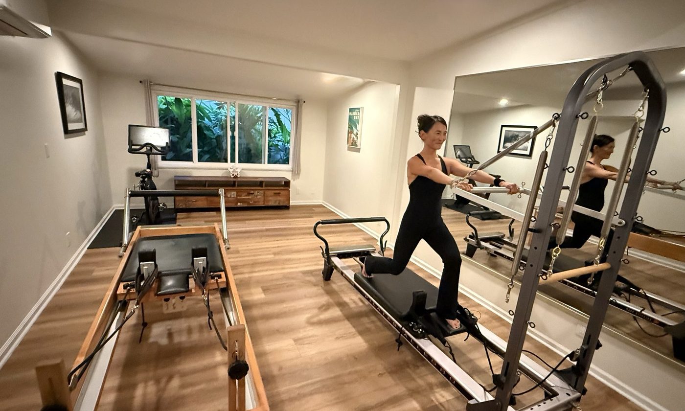Dr. Moon working on the Pilates tower in her home studio, with a second reformer and the mirrored wall behind her.